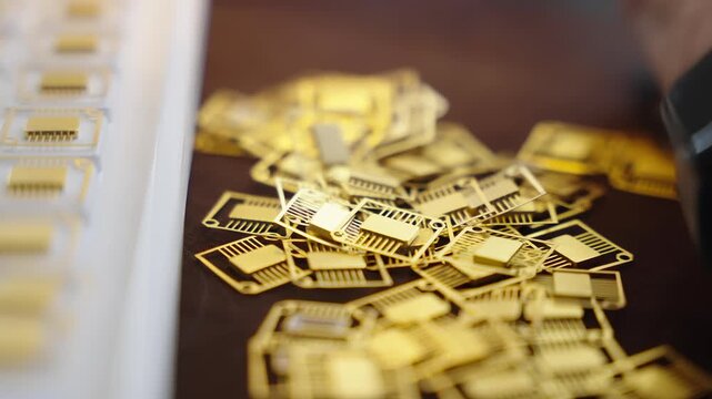 Close-up of gold-plated microchip leadframes scattered on a workbench beside a tray during electronics manufacturing, highlighting precision components and selective focus