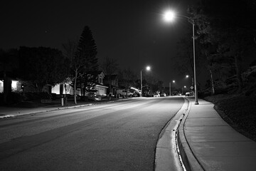 Quiet residential street at night in Corona, California, lit by streetlights with empty roadway, sidewalk, and suburban homes. © Savion