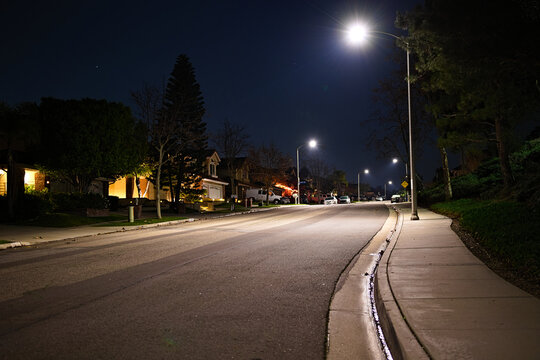 Quiet residential street at night in Corona, California, lit by streetlights with empty roadway, sidewalk, and suburban homes.