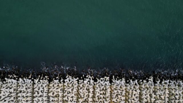 Aerial video of concrete tetrapods forming a breakwater as waves crash against the coast. Abstract geometric pattern, coastal protection infrastructure, sea and motion
