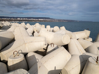Concrete wave breakers stacked along the shoreline, forming a massive coastal defense structure against sea waves. Industrial geometry, repetition, and texture at the water s edge