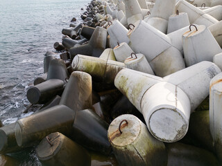 Concrete wave breakers stacked along the shoreline, forming a massive coastal defense structure against sea waves. Industrial geometry, repetition, and texture at the water s edge