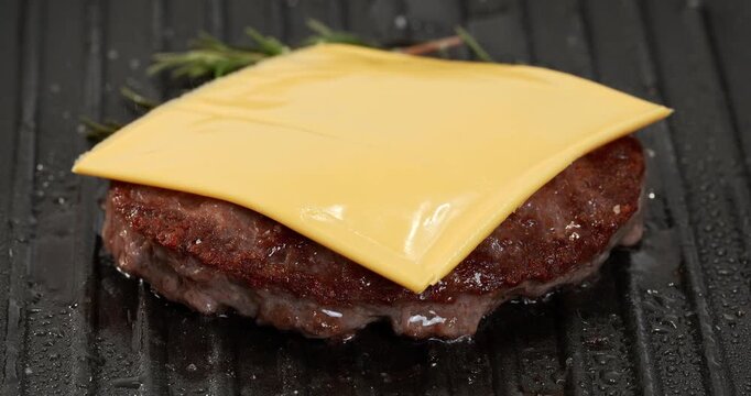 Raw beef burger patty with rosemary cooking, frying on grill pan, skillet. Cheese is placed on a cutlet that is fried.