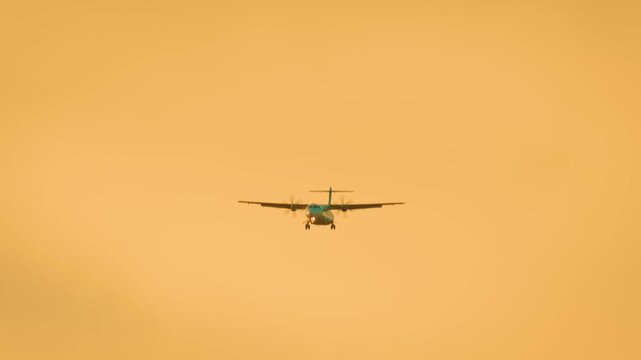 Propeller aircraft flying in golden sunset sky. Regional turboprop moving forward with landing gear down. Small passenger plane descending under warm atmospheric light. Twin engine propeller plane