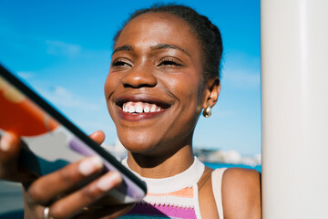 Close-up of smiling Black woman using smartphone for voice input. Emphasizes confidence, natural beauty, and personal connection through digital interaction in daily life.
