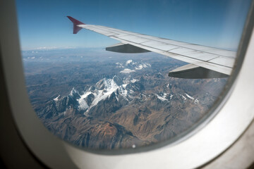 Airplane window framing the rugged, snow-capped peaks of the andes mountain range in peru during an aerial flight
