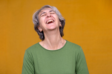 Senior woman with gray hair experiencing joy, giggling and showing happiness on a vibrant yellow...