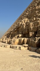 Visitors stand near the base of the Great Pyramid of Giza in Egypt. The sunlight shines on the stone blocks as they examine the ancient structure. The scene captures the pyramid's massive scale