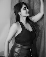 Black and white side profile portrait of a confident woman posing indoors against a textured fabric background. Elegant female model wearing a modern sleeveless top and skirt © Vivek