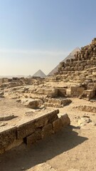 Tourists walk through the ancient ruins near the pyramids in Egypt. The sun shines bright while many explore the large stone structures and pathways around them