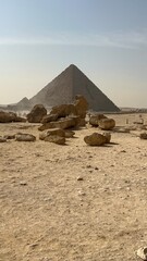 The pyramid structure rises in the background with large rocks scattered in the foreground. Dust fills the air and the sun shines in a clear sky above