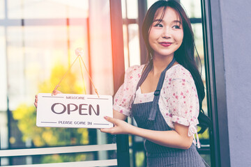 Female owner of coffee shop or restaurant turning round sign to open. Smiling young asian woman owner, employee retail coffee shop woman hand in setting sign board to open for welcome customer, reopen
