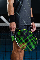 Midsection view of a male tennis player standing near the net holding a tennis racket on a blue court. Pause between points, focus, confidence and professional sport concept.