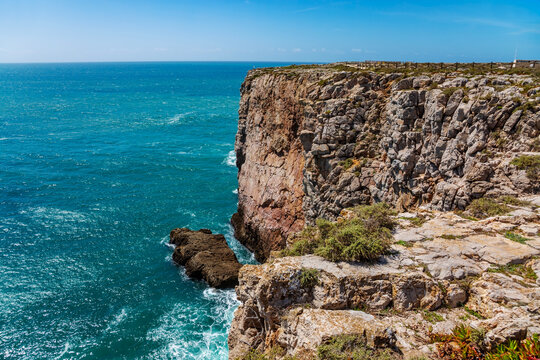 A stunning close-up view of the imposing cliffs at Cabo de S&atilde;o Vicente in Sagres, Portugal, where jagged rock formations plunge dramatically into the deep blue Atlantic Ocean.
