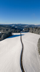 Obraz premium Winding road passing through deep snow in the Black Forest mountains, aerial view
