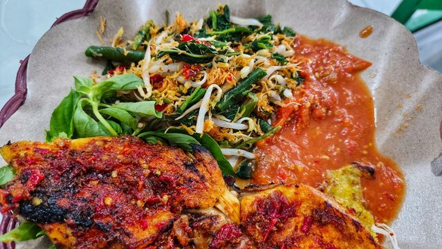 Indonesian grilled chicken known as ayam bakar served with urap vegetable salad and spicy sambal on paper lined plate for traditional culinary concept