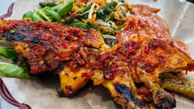 Indonesian grilled chicken known as ayam bakar served with urap vegetable salad and spicy sambal on paper lined plate for traditional culinary concept