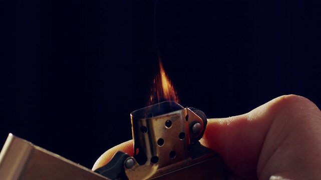 Close up of a metal lighter sparking and igniting a flame in slow motion on black background.