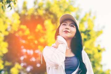 Asian woman wearing wireless headphones, smiling while relaxing in a park after workout and stretching, enjoying music and peaceful outdoor moment of contentment and well-being. 