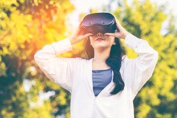 Asian woman wearing wireless headphones, smiling while relaxing in a park after workout and stretching, enjoying music and peaceful outdoor moment of contentment and well-being. 