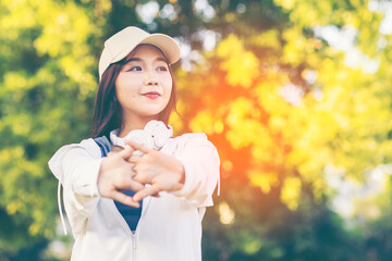 Asian woman wearing wireless headphones, smiling while relaxing in a park after workout and stretching, enjoying music and peaceful outdoor moment of contentment and well-being. 