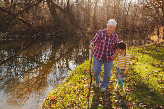 Smiling woman walking by a river holding hands with her granddaughter on an autumnal day