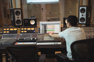 Asian male audio engineer operating mixing console in studio control room with speakers, copy space