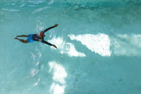 African American man floating on back in turquoise pool wearing trunks and rash guard, copy space
