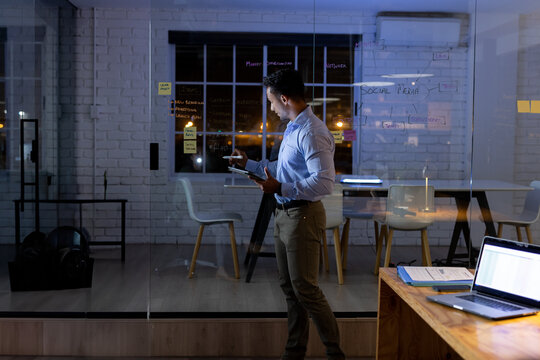 Businessman writing on glass whiteboard with sticky notes at office holding tablet next to laptop