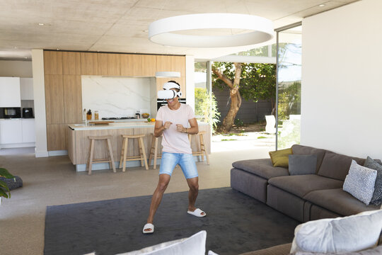 Asian man practicing boxing stance wearing VR headset on gray rug near wooden kitchen island