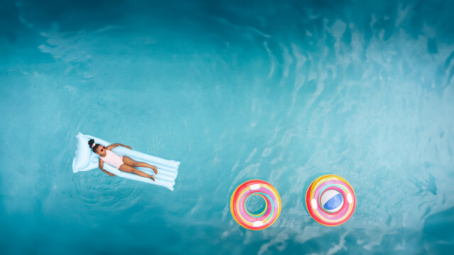 Child relaxing on pool float with colorful rings and ball nearby in water