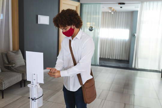African American man dispensing hand sanitizer at lobby wearing red face mask with crossbody bag