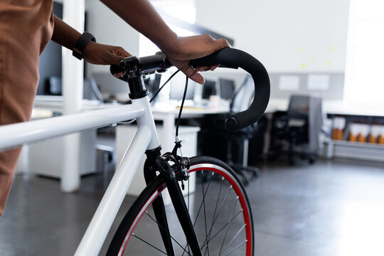 African American woman gripping bicycle handlebars standing in open-plan office among desks binders
