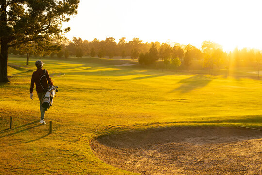 African American golfer striding on fairway with golf bag by sand bunker, tee markers, copy space