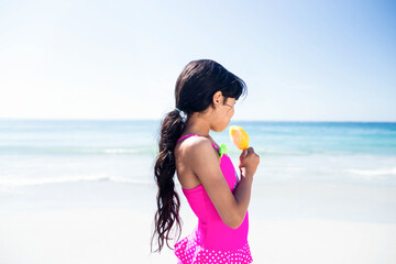 Obraz premium Girl holding orange popsicle, standing on beach near turquoise sea, wearing pink polka dot swimsuit