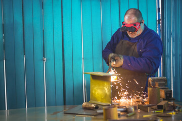 Senior man operating angle grinder against I-beam at metal workbench with sparks, copy space