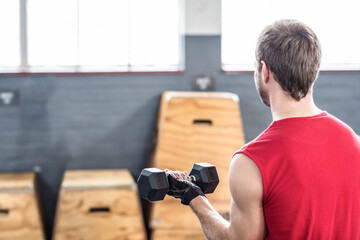 Man wearing lifting gloves, lifting black hex dumbbells in gym with wooden plyo boxes, copy space