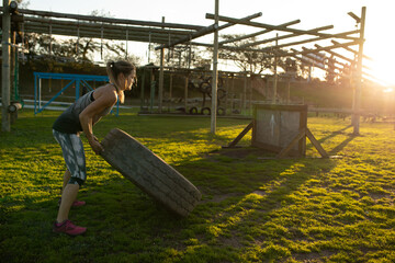 White female athlete wearing gymwear flipping tractor tire on obstacle course at sunset, copy space