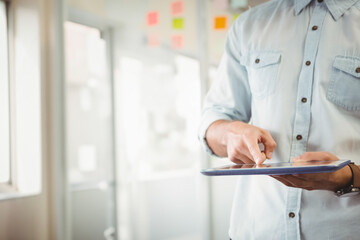Adult man in blue shirt holding tablet near sticky notes on glass in office, copy space