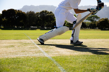 Male cricketer wearing white uniform playing shot on pitch holding cricket bat with gloves and pads