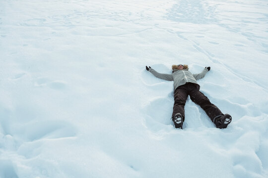 Woman making snow angel on fresh snow field wearing winter jacket and boots, copy space