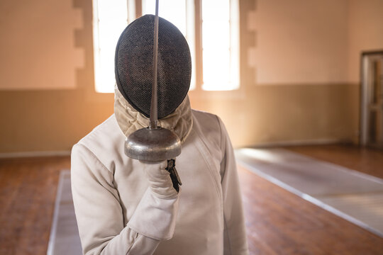 African American female athlete fencing on gymnasium floor wielding epee and wearing fencing mask