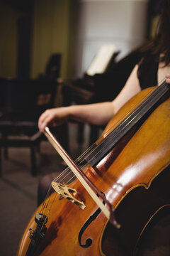 Female musician holding cello bow drawing across strings in rehearsal hall beside grand piano