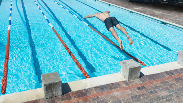 Male athlete diving into lane at outdoor pool in black jammers with floating dividers, copy space