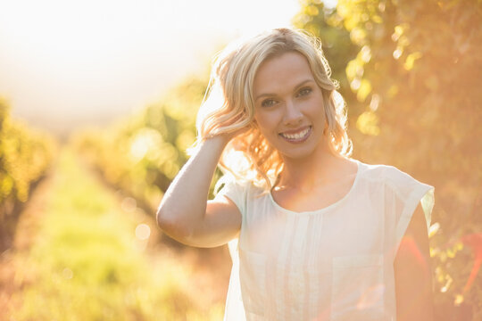 Blonde woman standing between grapevine rows soaking in golden-hour light and creating lens flares