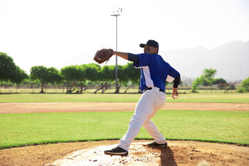 Male pitcher wearing uniform winding up on dirt mound at ballpark holding glove and baseball