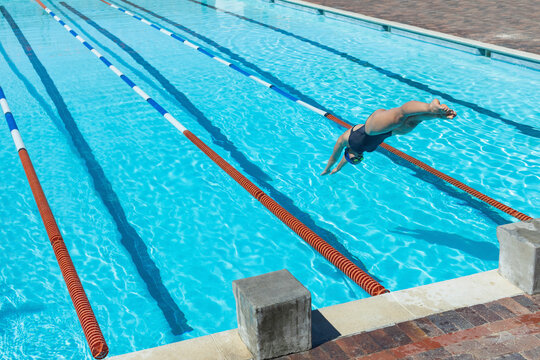 Female swimmer diving into outdoor lap pool wearing swimsuit, swim cap by lane lines, copy space