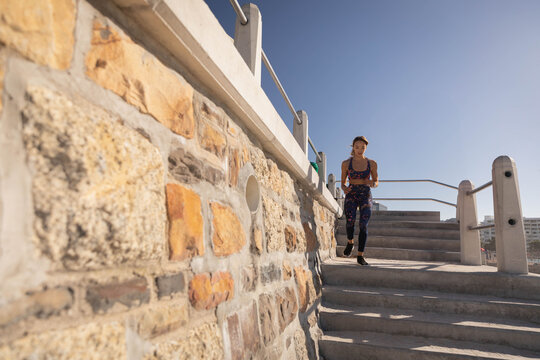 Asian woman running down concrete steps along seaside stone wall and metal handrails, copy space