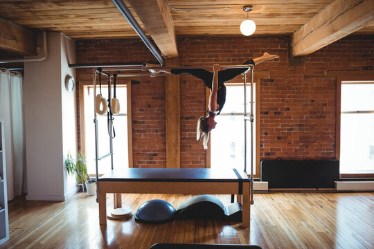 Mid adult woman performing inverted split on Pilates Cadillac in fitness studio with Pilates rings