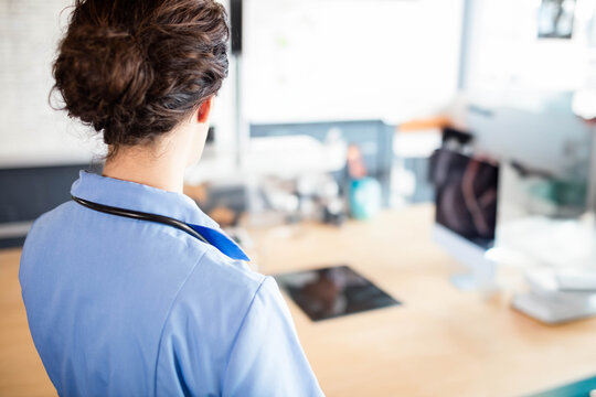Female nurse standing at office desk checking stethoscope and reviewing tablet data, copy space